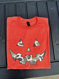 “Orange Gildan Softstyle t-shirt with camo jack-o’-lantern face design”